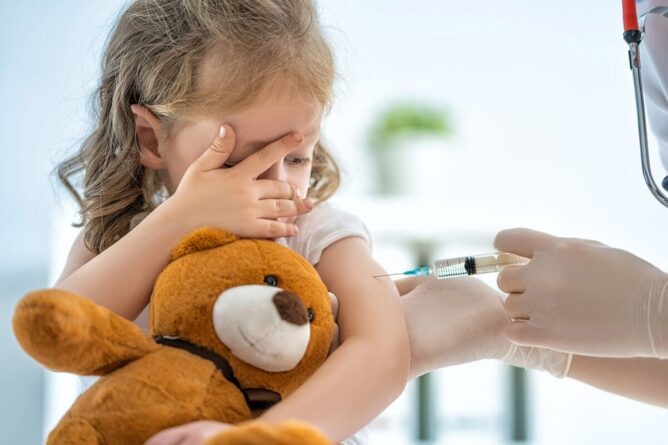 девочка с плюшевым медведем в руках получает прививку