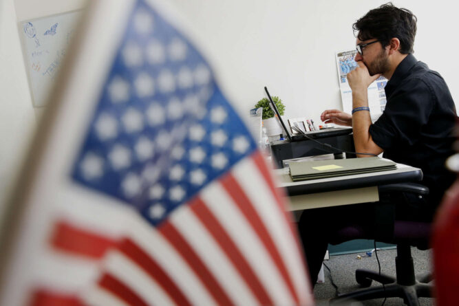 мужчина в очках работает за компьютером на фоне флага США