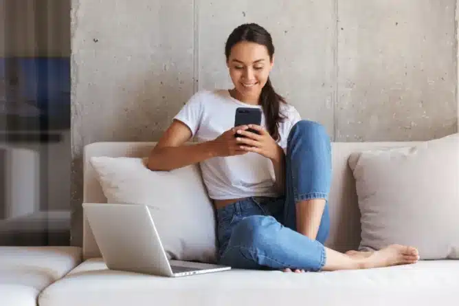 девушка сидит на диване с телефоном и ноутбуком