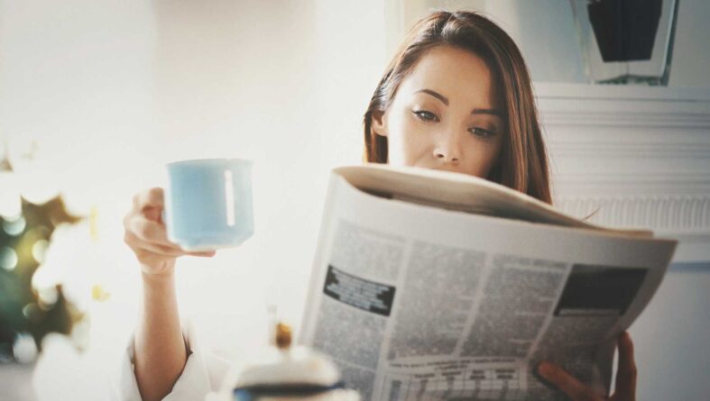 девушка читает газету с чашкой в руке